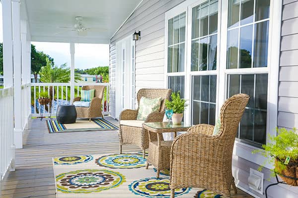 Large wooden porch with wicker chairs, outdoor rugs and plants overlooking Lake Rexmere.
