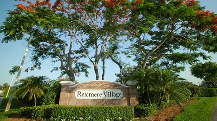 Brick and limestone entrance and sign to Rexmere Village, surrounded by flowers, trees and small palm trees