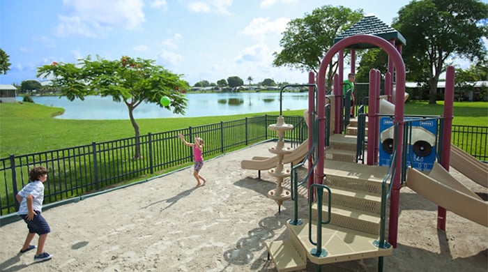 Playground overlooking Rexmere Lake on a sunny day, children playing catch with a playground ball