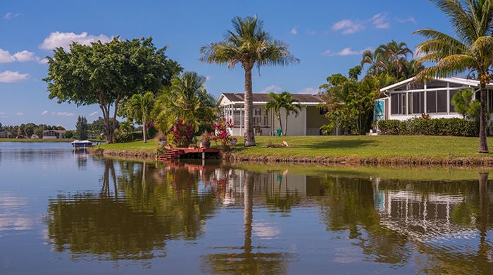 Rexmere lot on Rexmere lake with reflections of large homes, palm trees and a small dock.