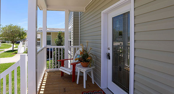 Covered front porch of Seaglass Sanctuary featuring a decorative beveled-glass entry door, white railings, coastal-style seating, and an inviting outdoor entrance.